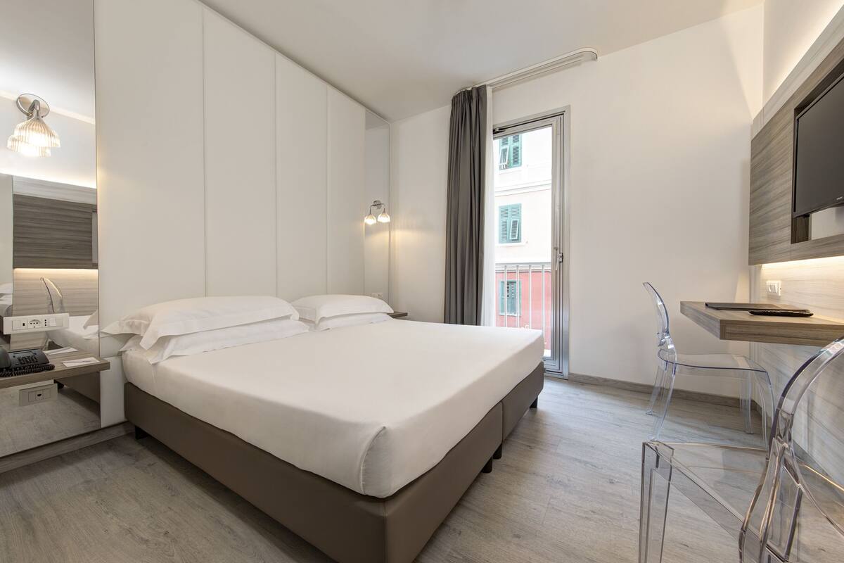 A modern hotel room with a large bed, a desk with a chair, and a TV mounted on the wall.