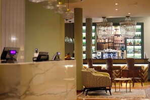A lobby with a reception desk, patterned chairs, a bar area with bookshelves, and chandeliers.
