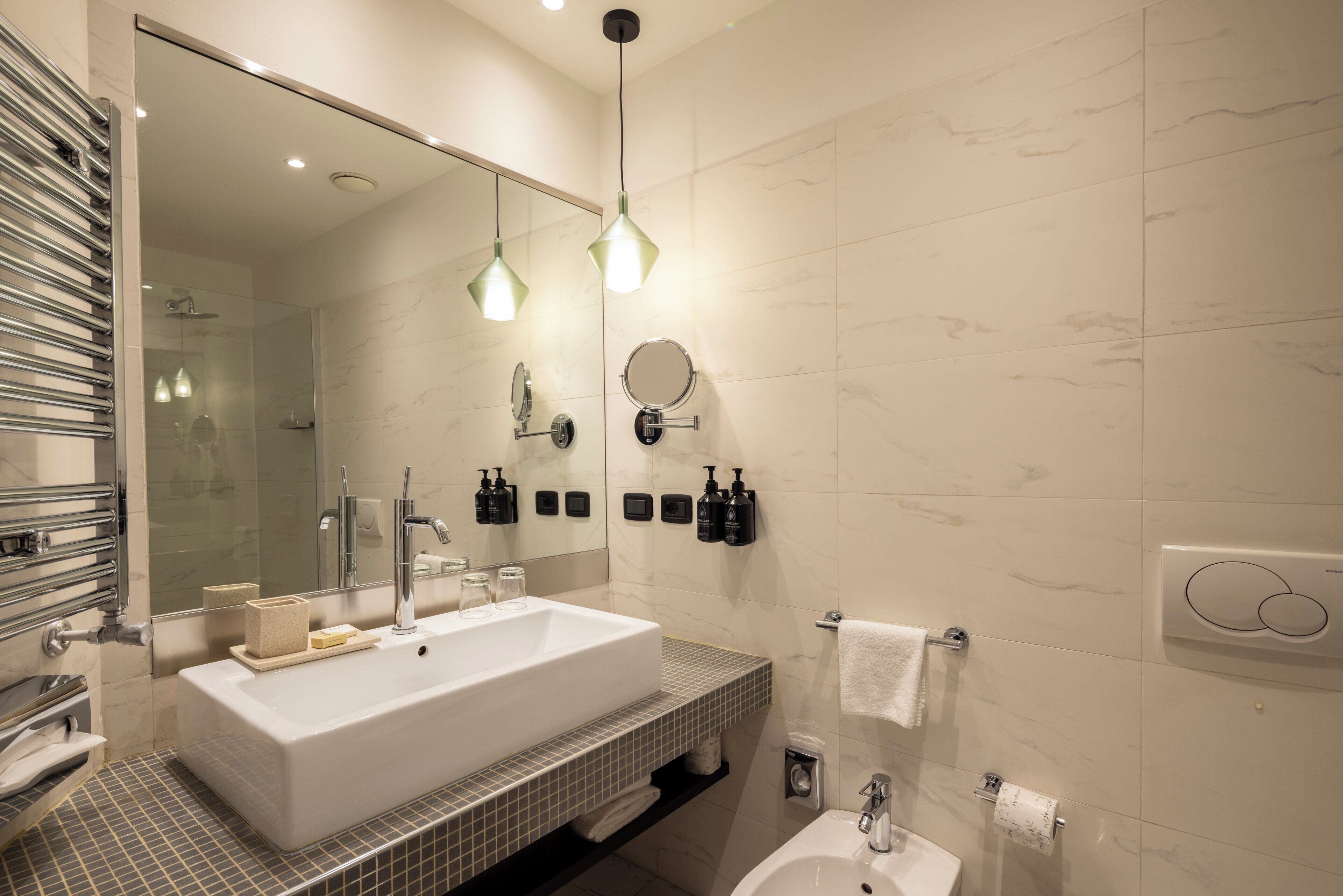 A modern bathroom with a large white sink, a mirror, and two pendant lights.