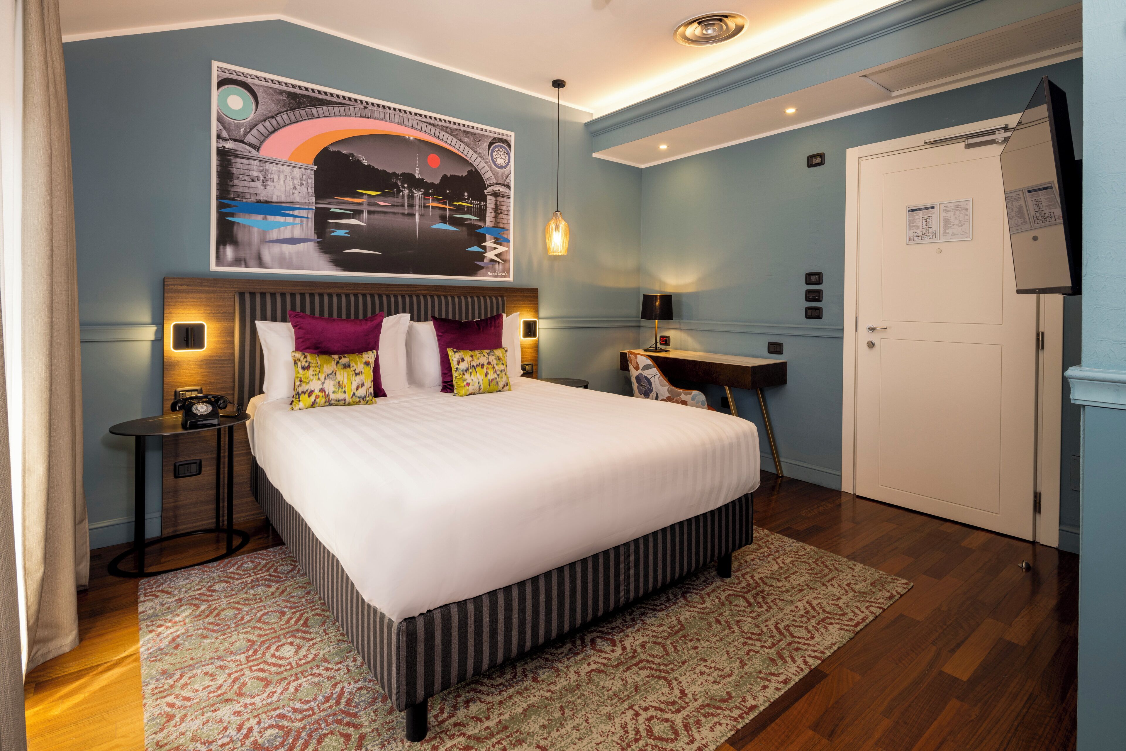 Ein Hotelzimmer mit einem großen Bett, einem Nachttisch, einem Schreibtisch und einer Tür.