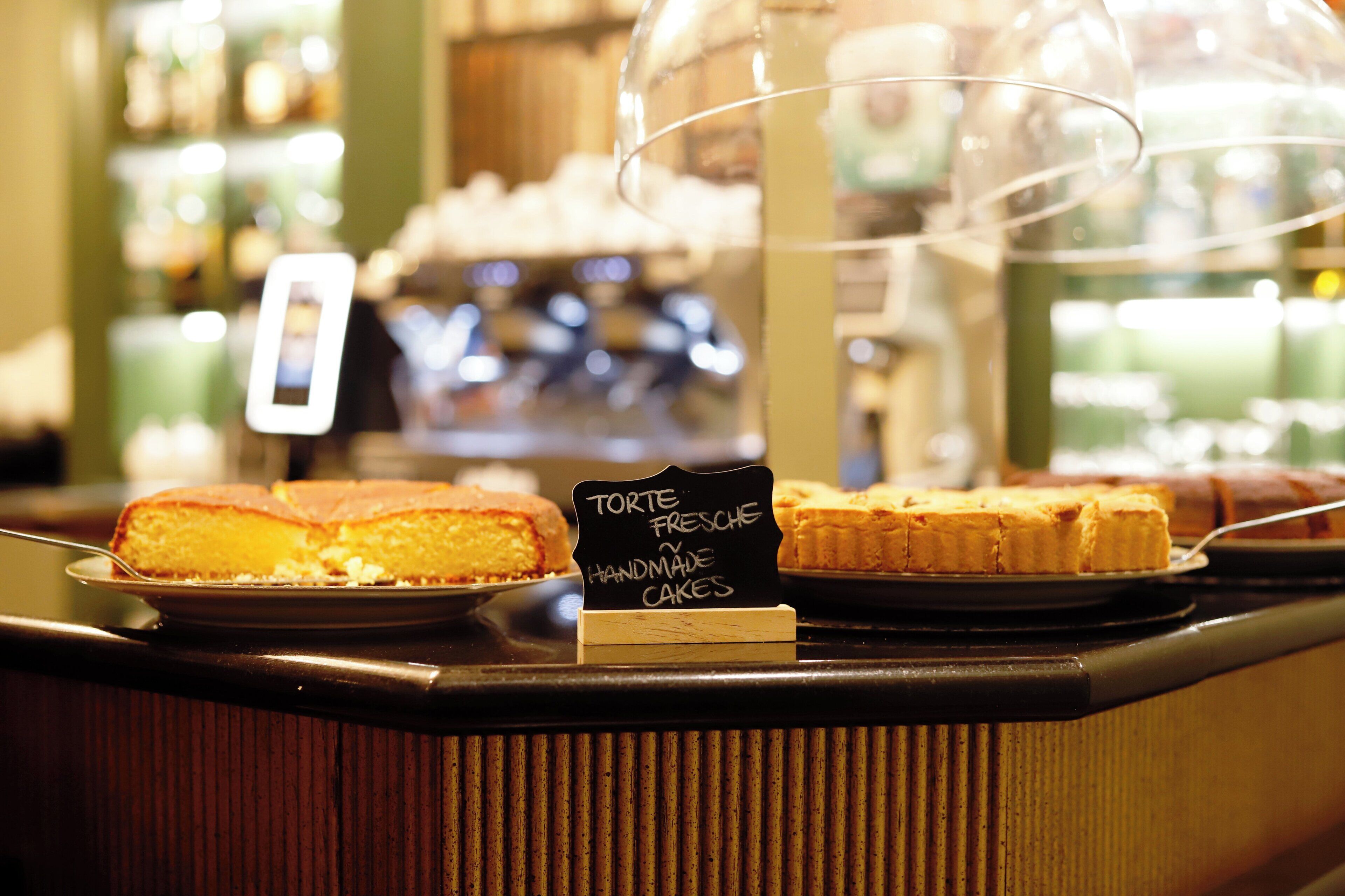 Eine Kuchendisplay mit Kuchen und einem Schild, das 'Torte Fresche Handmade Cakes' anzeigt.