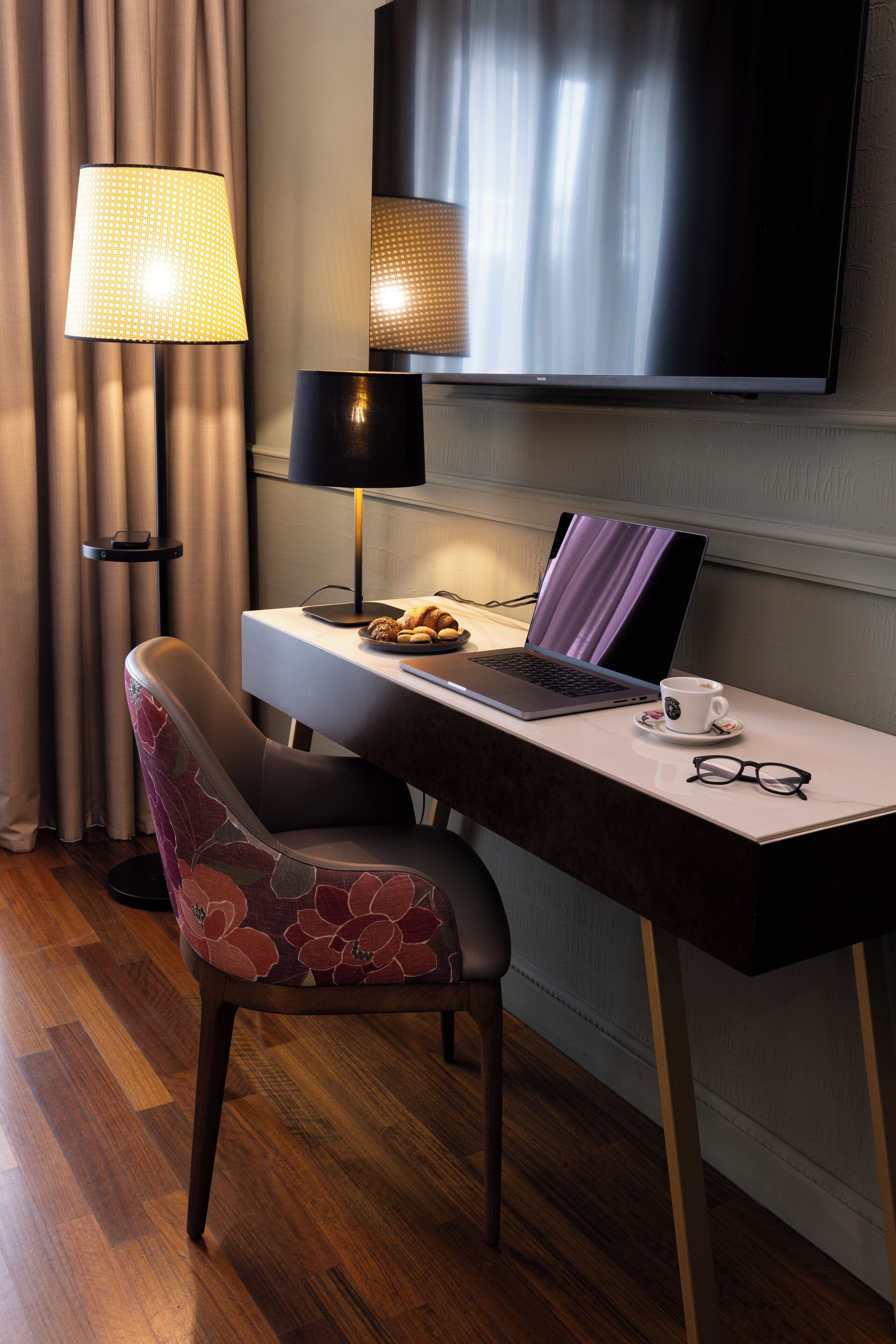 Ein Hotelzimmer mit Schreibtisch, Laptop, Kaffeetasse und einer Brille.