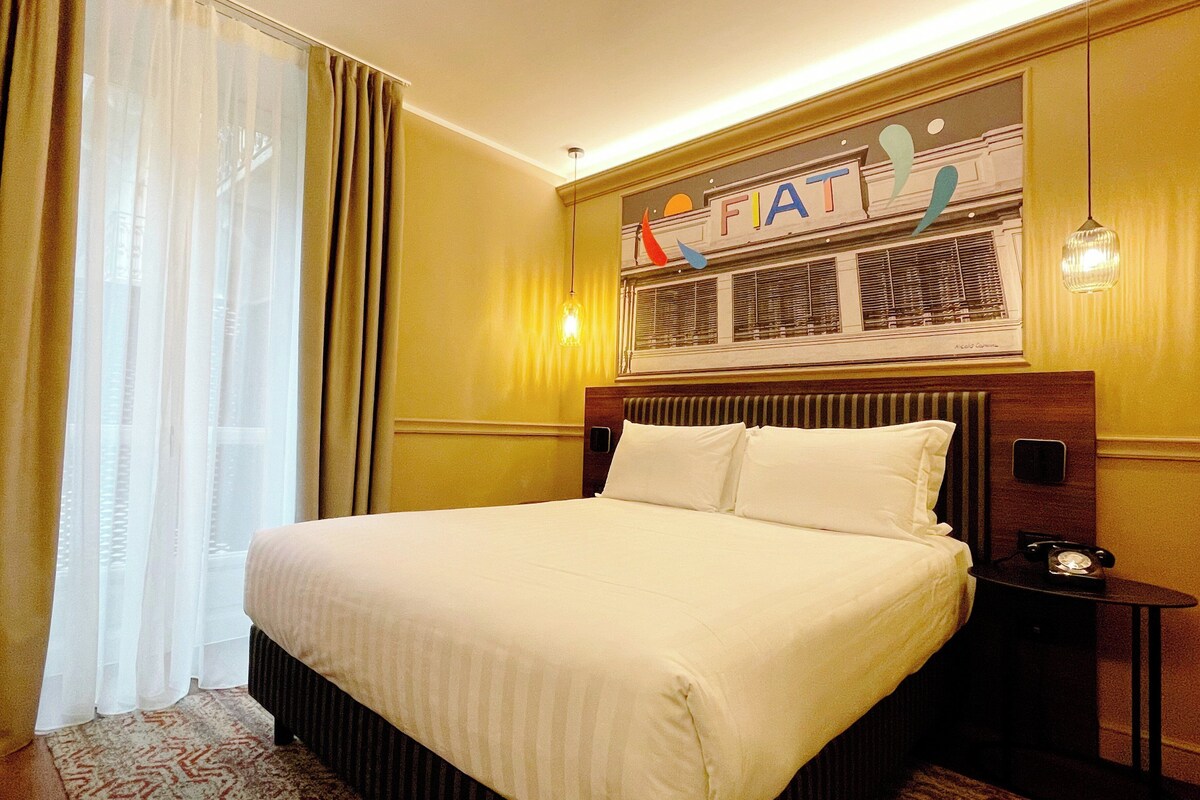 Habitació d'hotel amb un llit gran, una nit taula amb un telèfon i una finestra amb cortines.