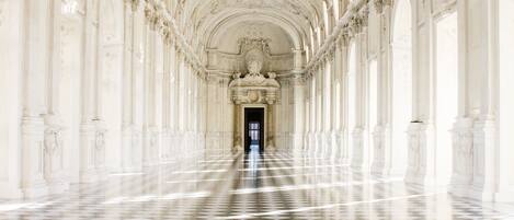 Un long couloir orné de colonnes blanches et doté d’un sol à carreaux.
