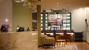 A lobby with a reception desk, patterned armchairs, a bar area with a bookshelf, and a chandelier. - Hotel Indigo Turin by IHG (Turin)