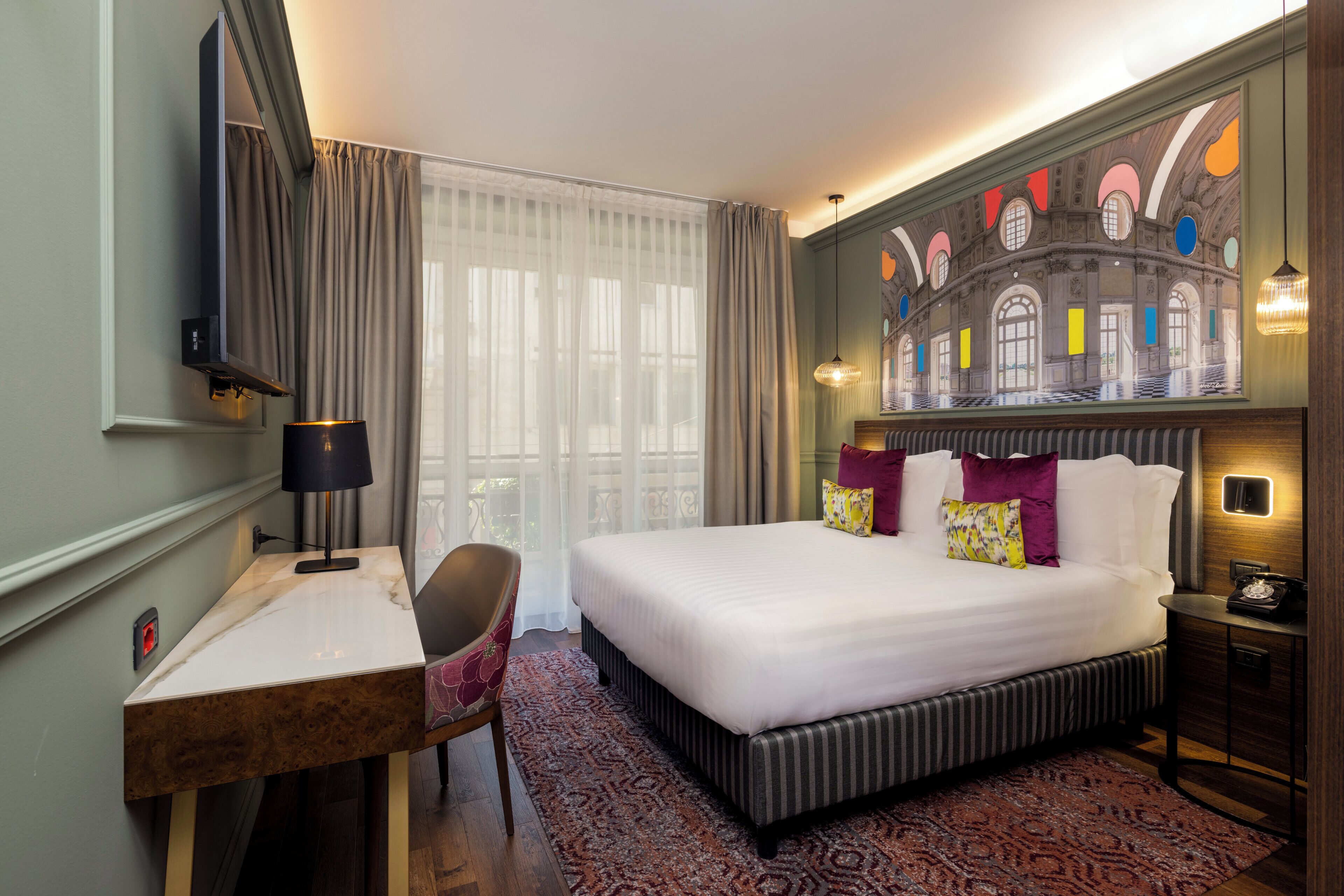 A hotel room with a large bed, a desk, a chair, a desk lamp, a telephone, and a painting on the wall.