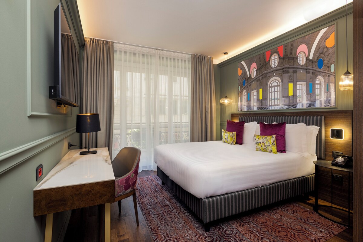 Habitación de hotel con una cama grande, un escritorio, una silla, una lámpara de escritorio, un teléfono y un cuadro en la pared.
