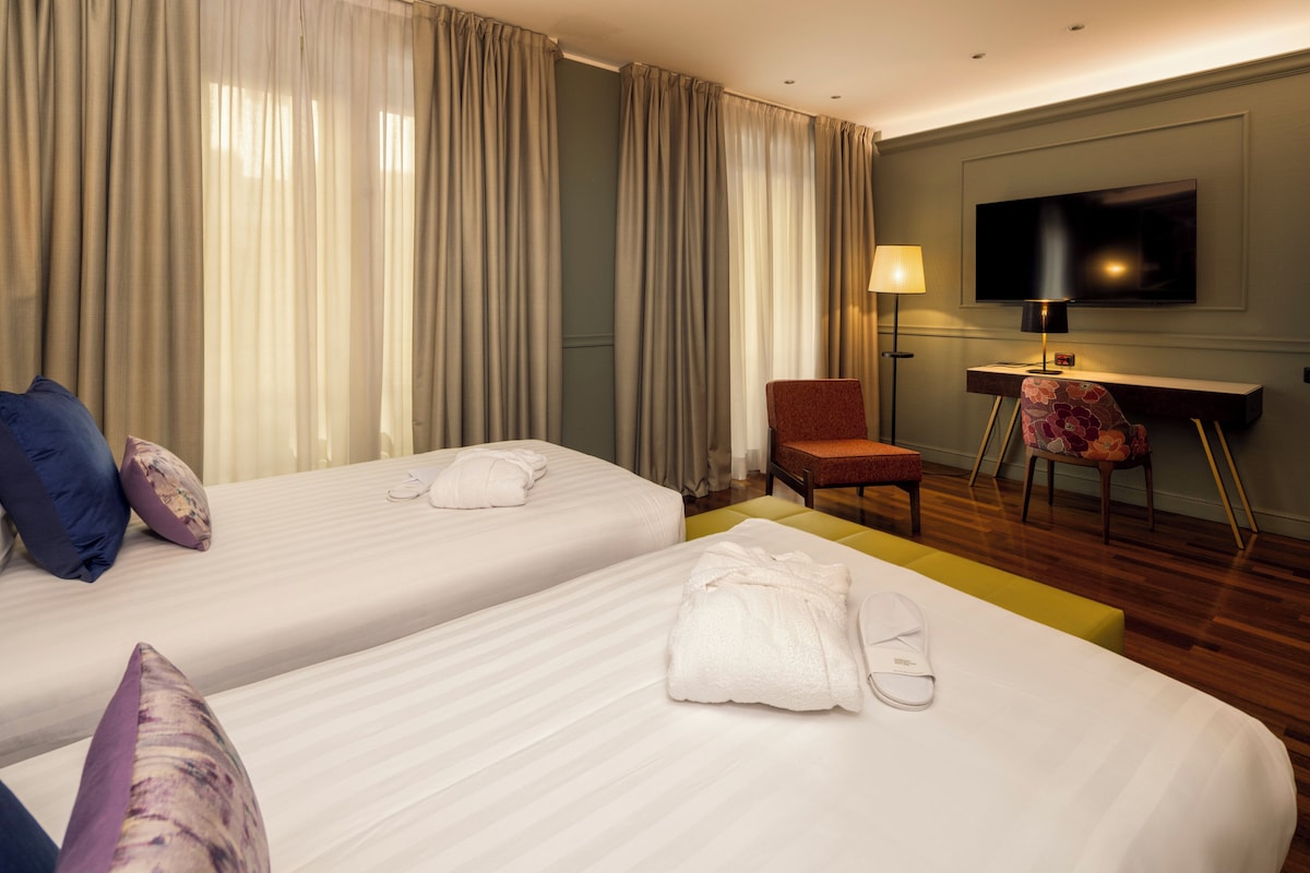 Una habitación de hotel con dos camas, un escritorio, una silla, un televisor y una lámpara.