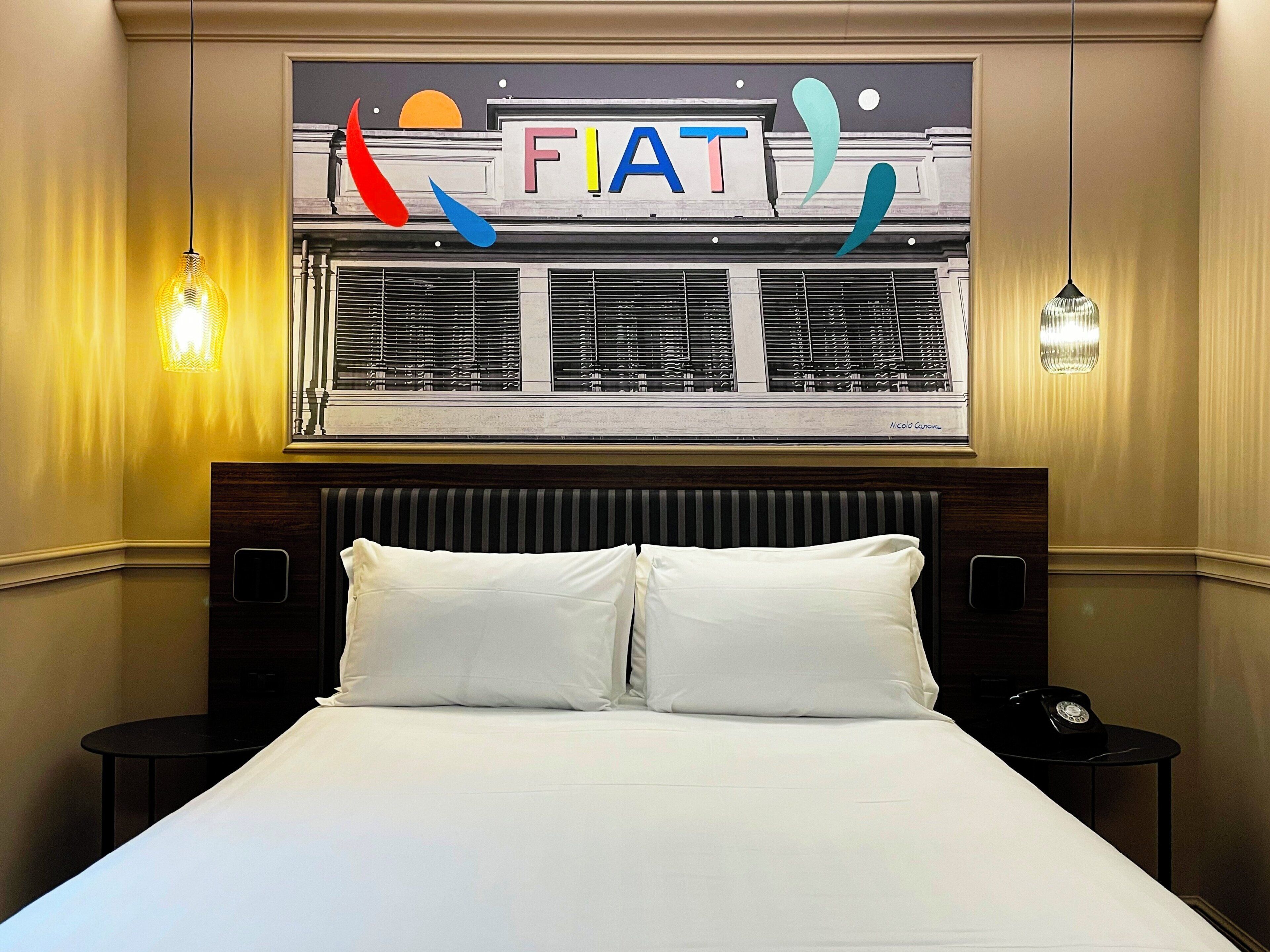 Een hotelkamer met een bed, twee nachtkastjes, een raam met zonwering en een bord boven het raam.