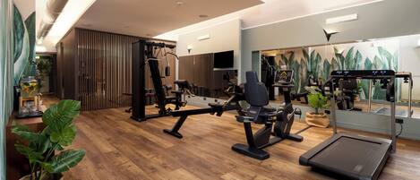 Un gimnasio moderno con suelo de madera, equipamiento de ejercicio y espejos amplios.
