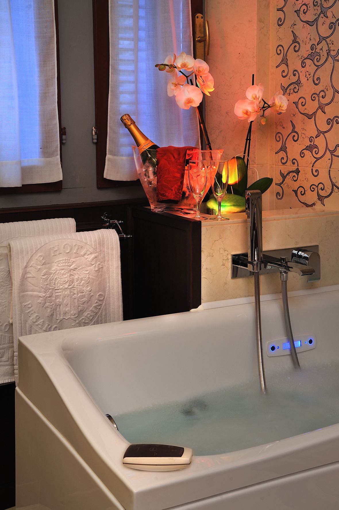A bathroom with a bathtub, a bottle of champagne, and orchid flowers.