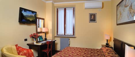 Una habitación de hotel con una cama, un escritorio con computadora, una silla, una ventana con cortinas y obras de arte en las paredes.
