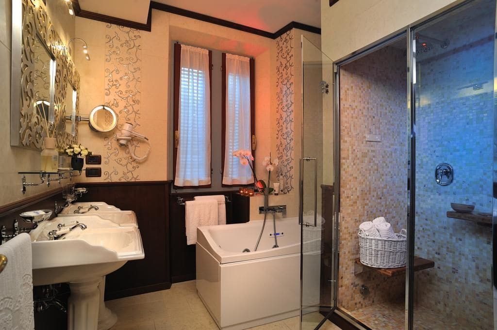 Ein Badezimmer mit zwei Waschbecken, einer Badewanne, einer Duschkabine aus Glas und einem Waschtisch mit Spiegel und Handtuchhalter.