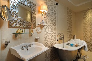 Un baño con un espejo grande, dos lavamanos, una bañera y un aplique de pared.