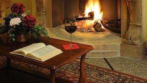Una chimenea con fuego, un libro sobre una mesa y un jarrón con flores.