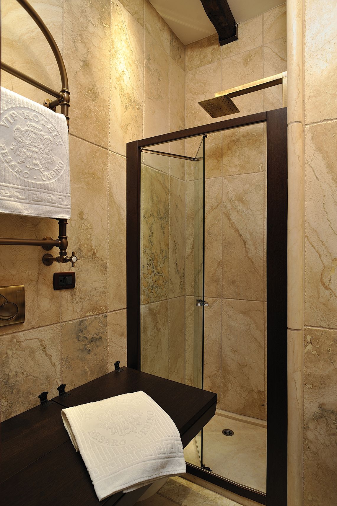 A modern bathroom with a glass-enclosed shower, marble walls, and a black countertop with a towel.