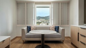 Una sala de estar moderna con un sofá, una mesa redonda y vistas a un paisaje urbano a través de un amplio ventanal.