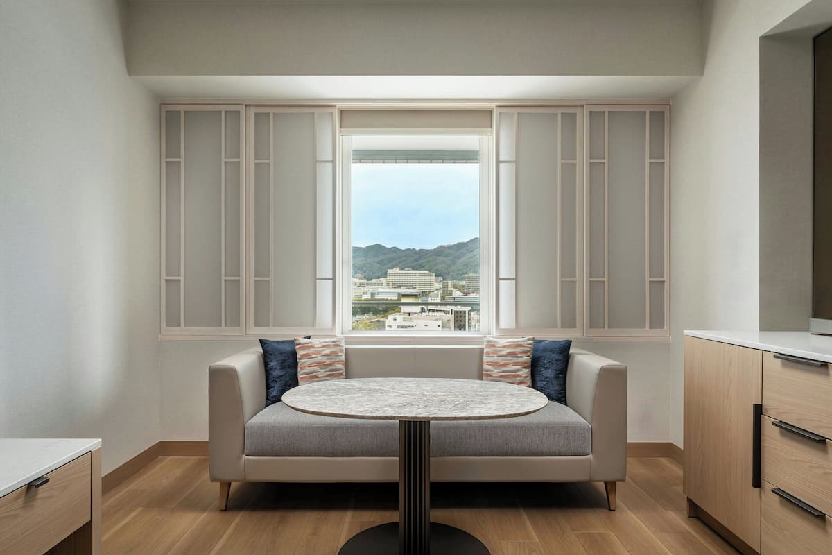 Una sala de estar moderna con un sofá, una mesa redonda y vistas a un paisaje urbano a través de un amplio ventanal.