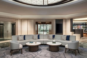 A modern lounge area with a curved sectional sofa, two round coffee tables, and a patterned carpet.