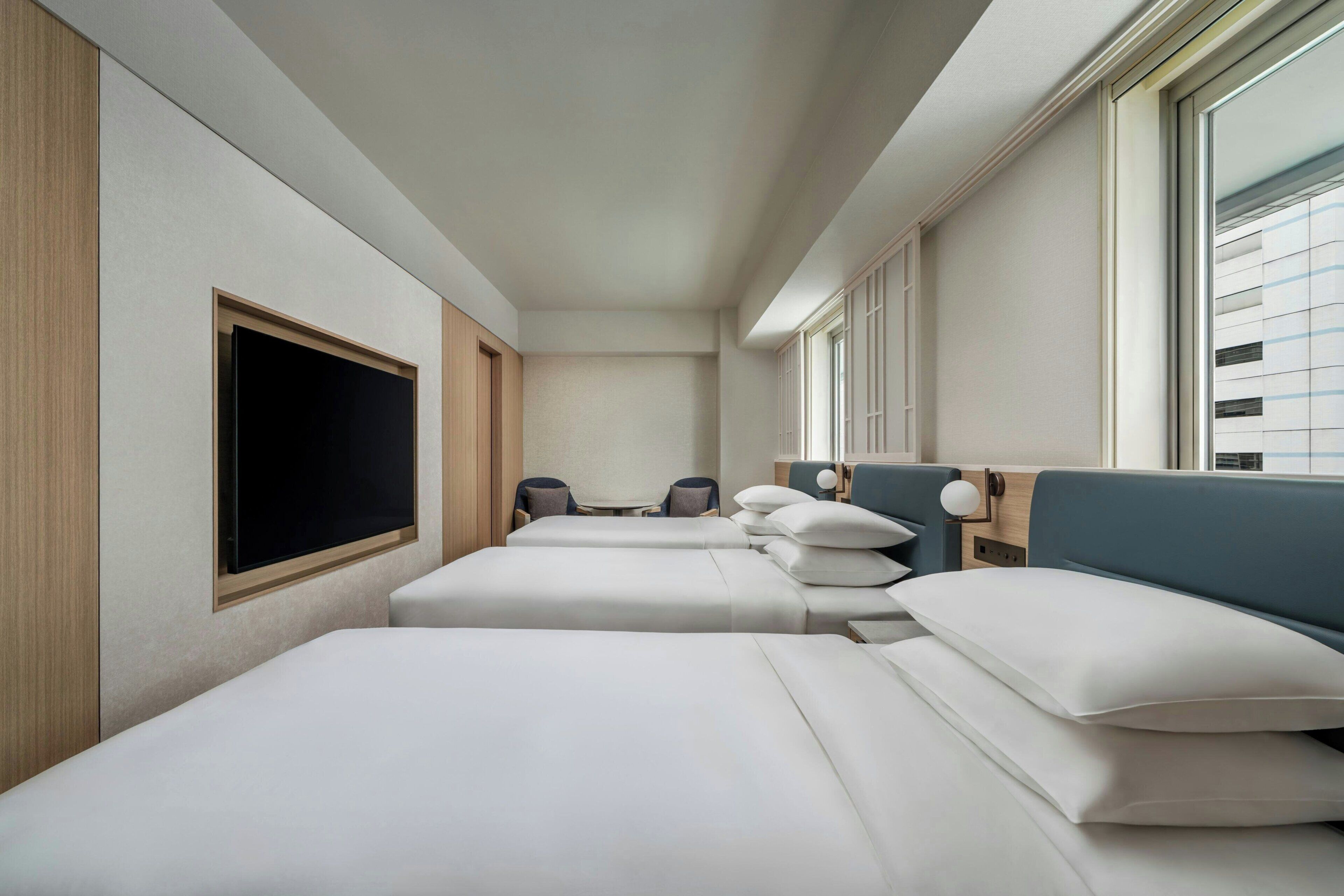 A hotel room with two beds, a TV, a desk, and a window.