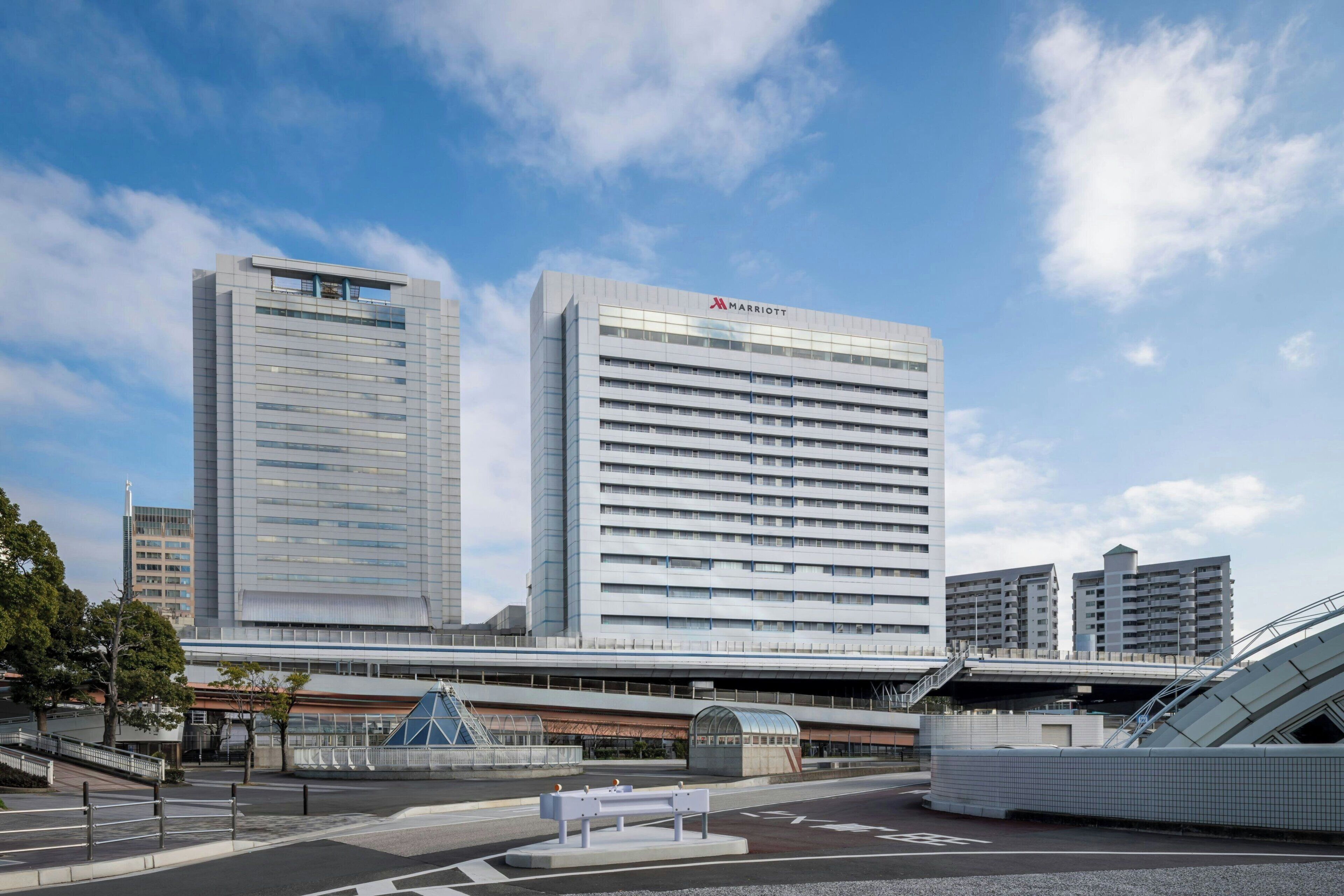 A modern hotel with a prominent Marriott logo, surrounded by urban infrastructure including a bridge and other buildings.