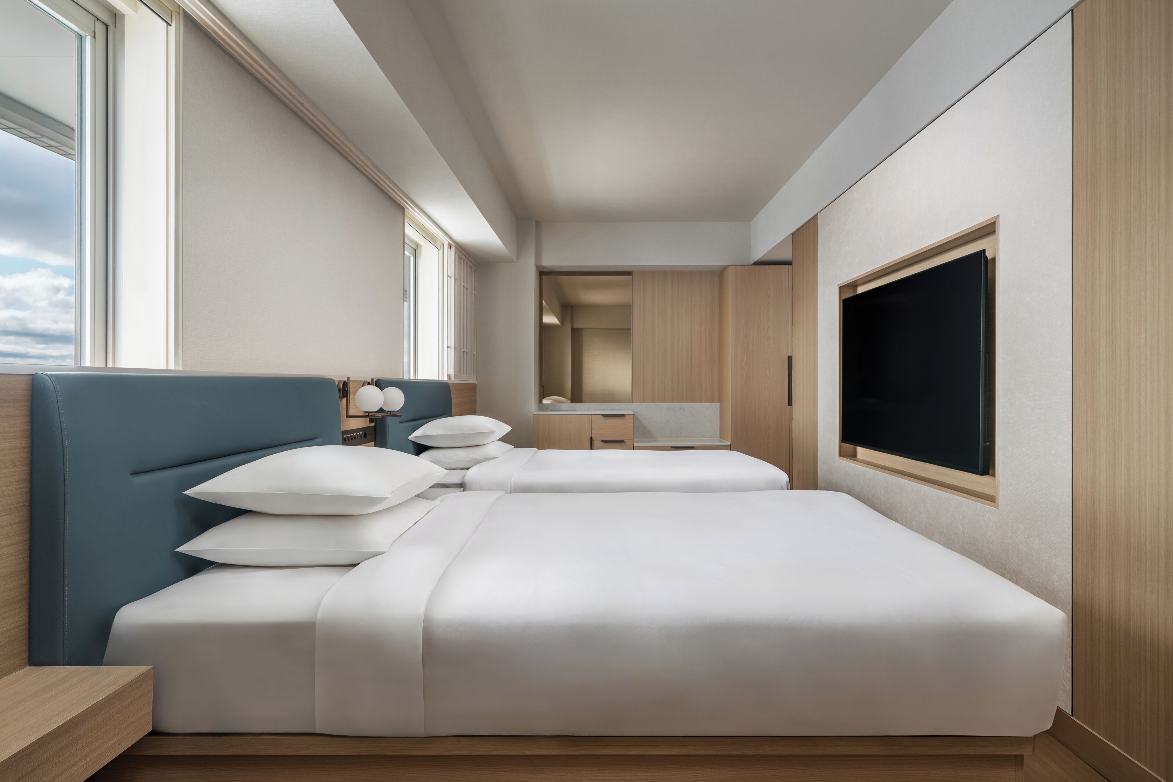 Quarto de hotel moderno com duas camas, televisão e vista para o céu.