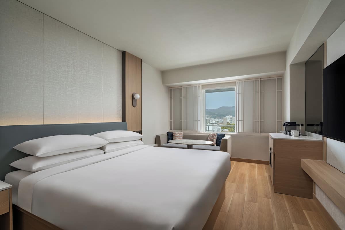 Una habitación de hotel moderna con una cama grande, una zona de estar, un escritorio y un ventanal con vistas a la ciudad.