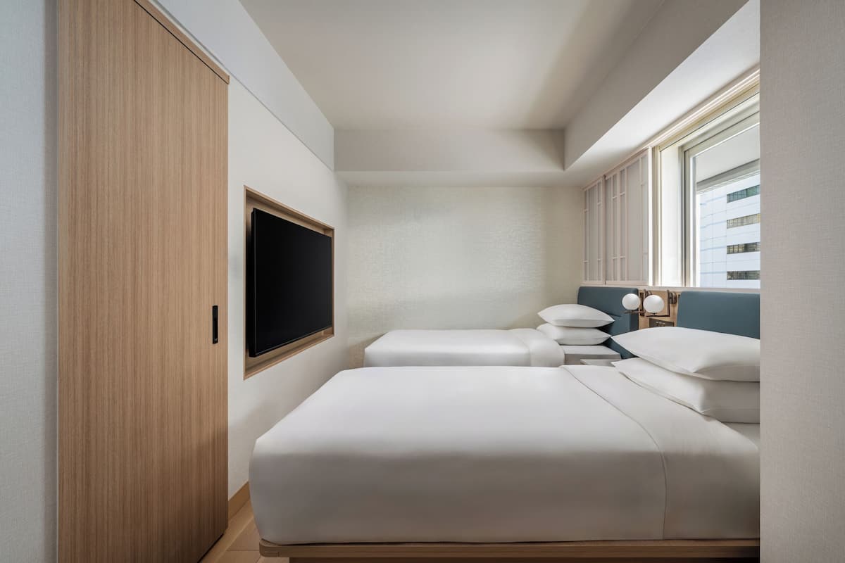 Un dormitorio con cama, mesitas de noche, televisor y ventana.