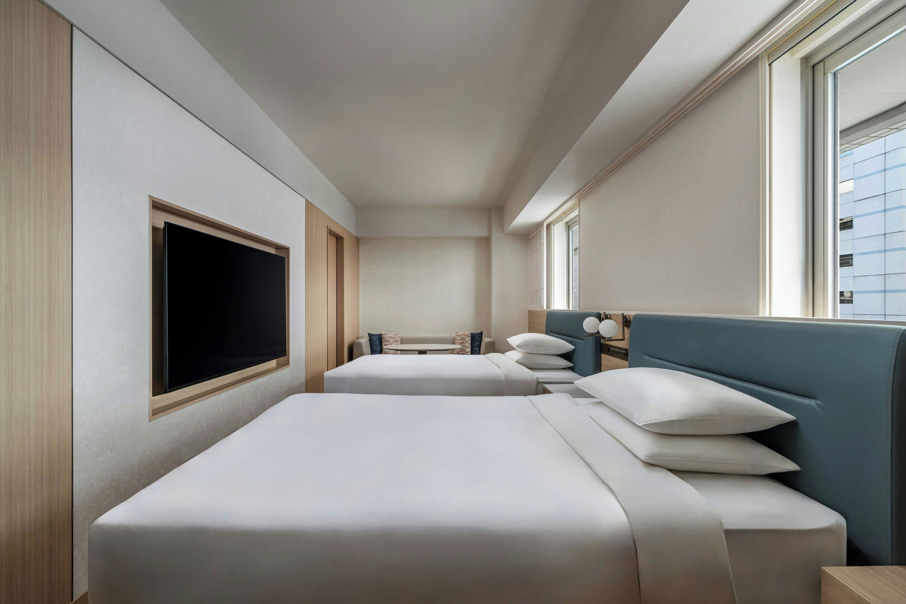 Ein Hotelzimmer mit zwei Betten, einem großen Fenster und Blick auf die Stadt.