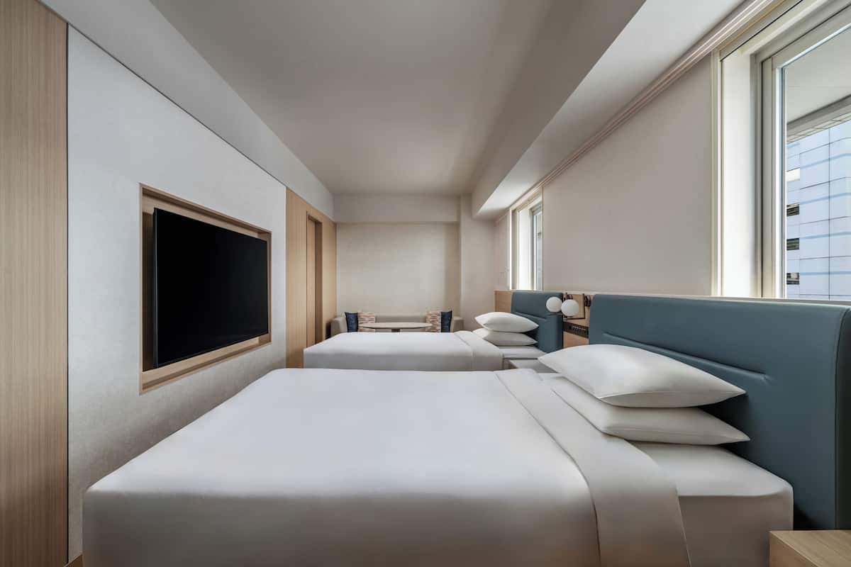 Habitación de hotel con dos camas, televisión, ventana y escritorio con lámpara.