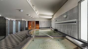 A modern indoor swimming pool with a checkered floor, a glass barrier, and a wooden door in the background.