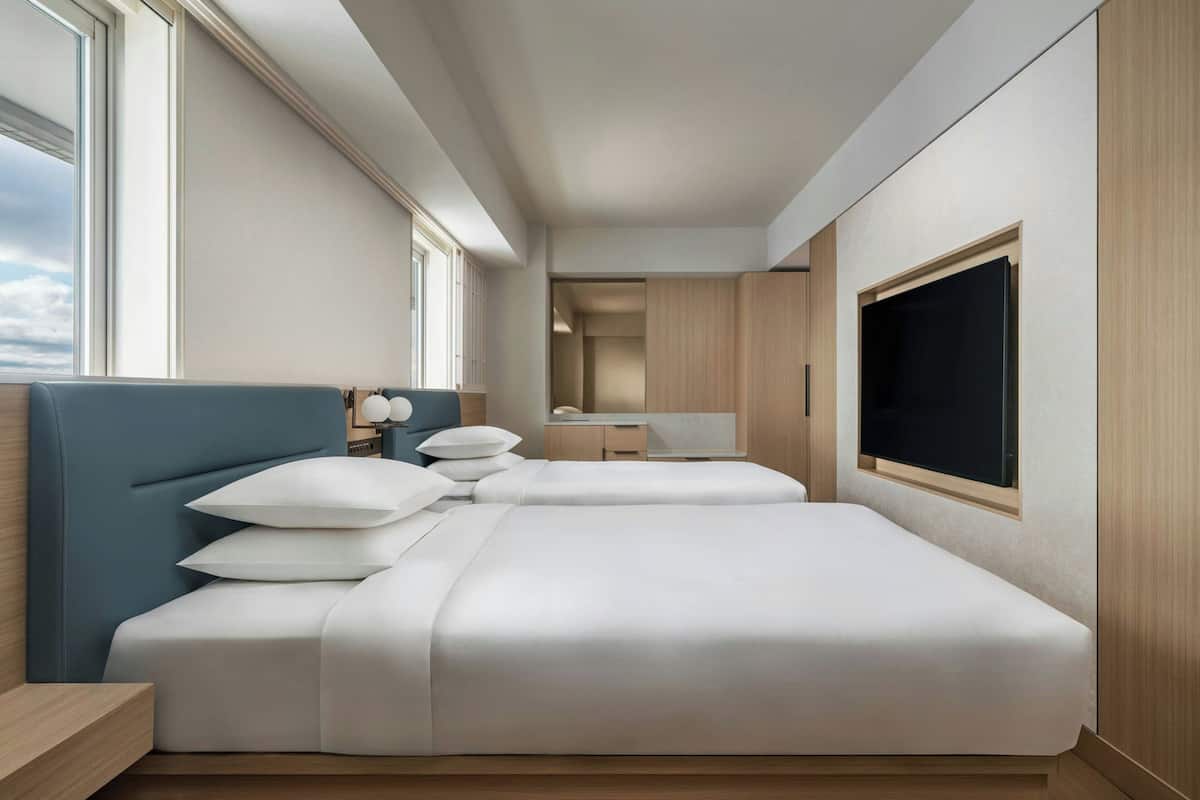 Una habitación de hotel moderna con dos camas, un ventanal grande, un televisor y un armario de madera.