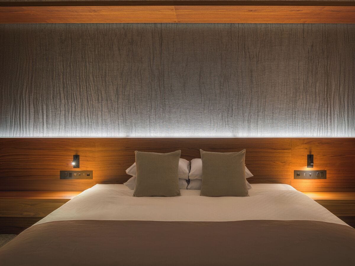 A neatly made bed with two pillows, a wooden headboard, and two wall-mounted light fixtures.