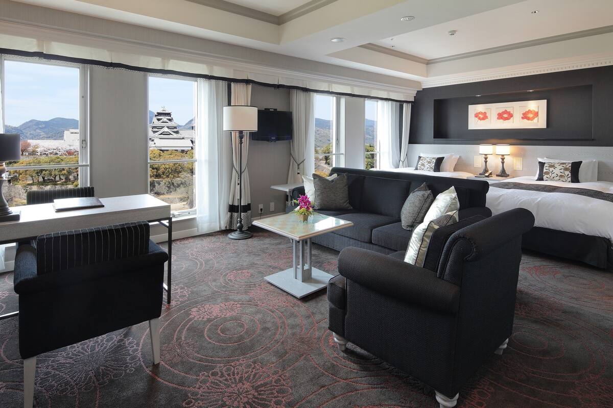 A hotel room with a bed, a sofa, a desk, and a TV.