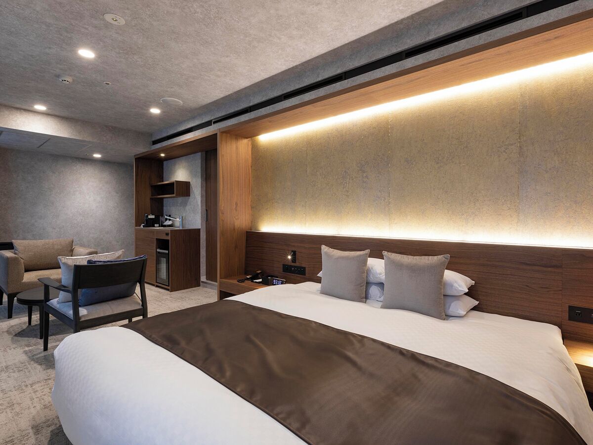 A modern hotel room with a large bed, a desk, and a sofa.