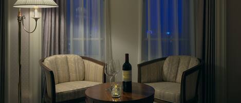 Habitación de hotel con dos sillones, una mesa redonda, una lámpara de pie y una botella de vino.