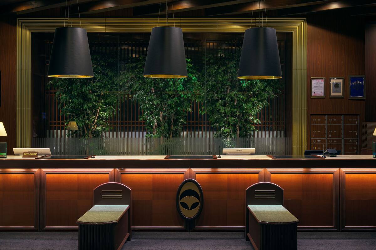 A reception desk with three pendant lights, a wooden reception area, a large window with a view of greenery, and a wall-mounted reception counter.
