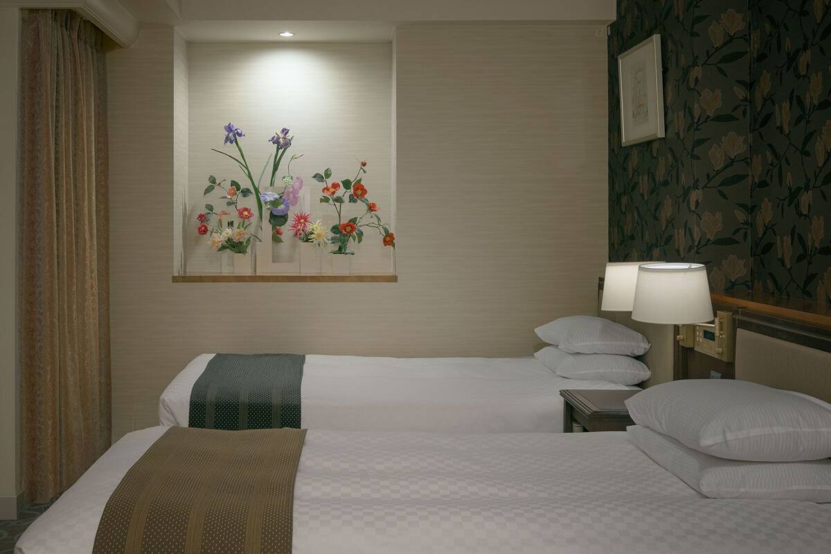 A hotel room with two beds, a floral artwork on the wall, a lamp, and a framed picture.