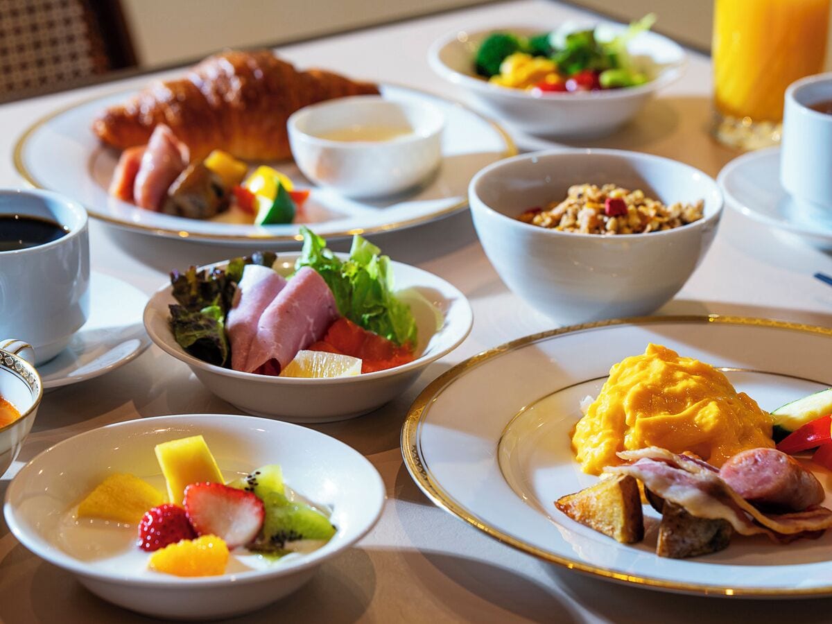 Ein Frühstückstisch mit verschiedenen Speisen, darunter Eier, Schinken, Toast und Obst.