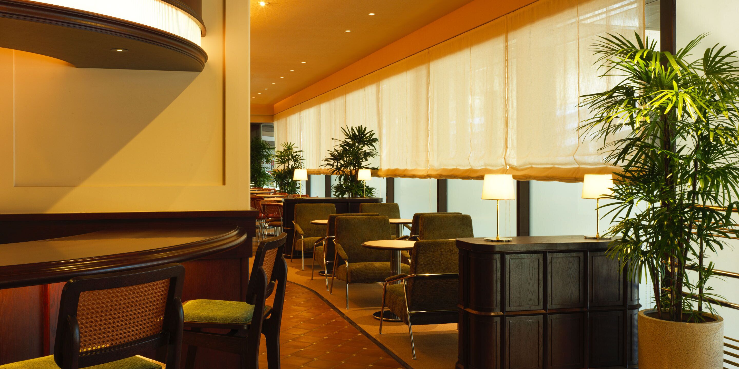 Vestíbulo de hotel con mostrador de recepción, zona de estar y amplios ventanales con cortinas.