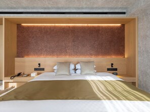 Ein modernes Hotelzimmer mit einem großen Bett, einem Holz-Kopfteil, Nachttischen und einer eingebauten Lichtleiste über dem Bett.
