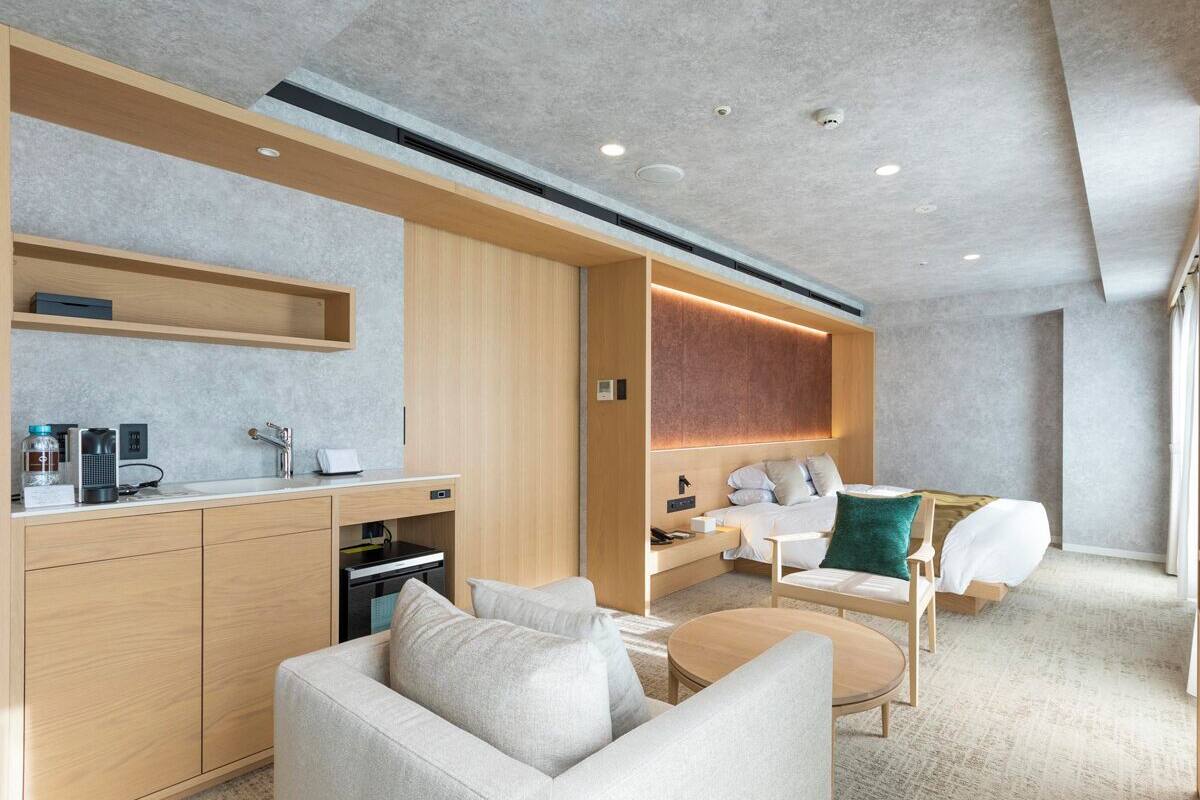 A modern hotel room with a kitchenette, a sofa, a bed, and a small table.
