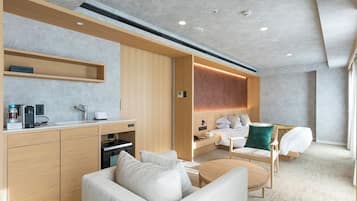 A modern hotel room with a kitchenette, a sofa, a bed, and a small table.