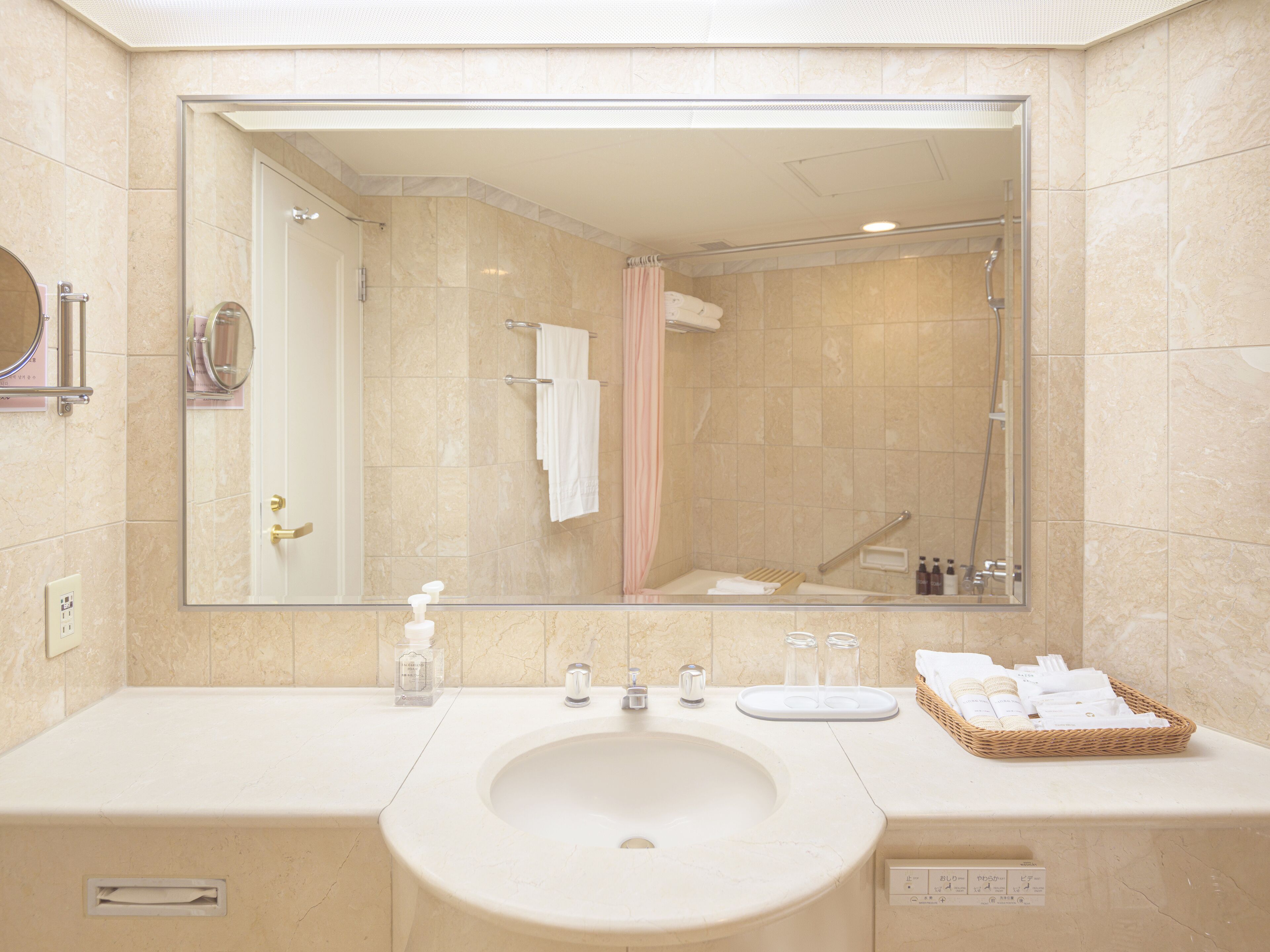 A bathroom with a large mirror, a sink, a shower, and a vanity with toiletries.