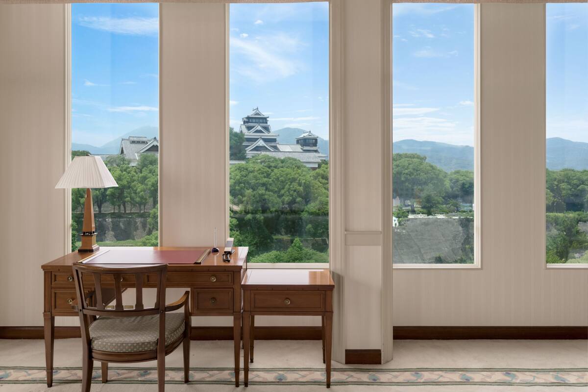 A room with a desk and chair, large windows with a view of traditional Japanese architecture.