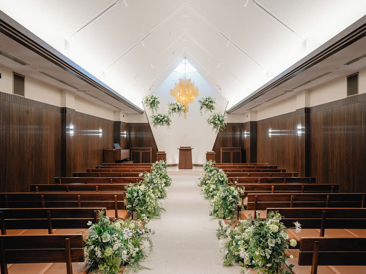 A church interior with wooden pews, a central aisle, and floral decorations.