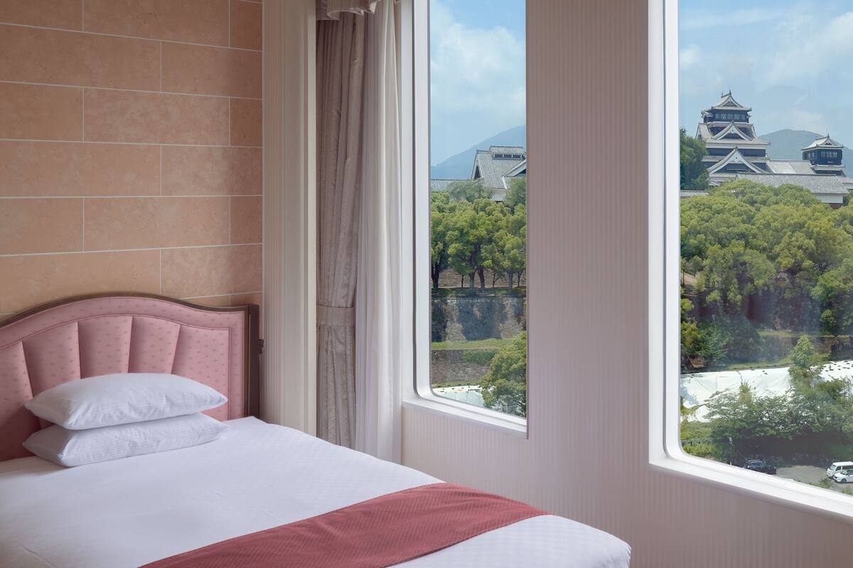 A hotel room with a large window offering a view of traditional architecture and trees.