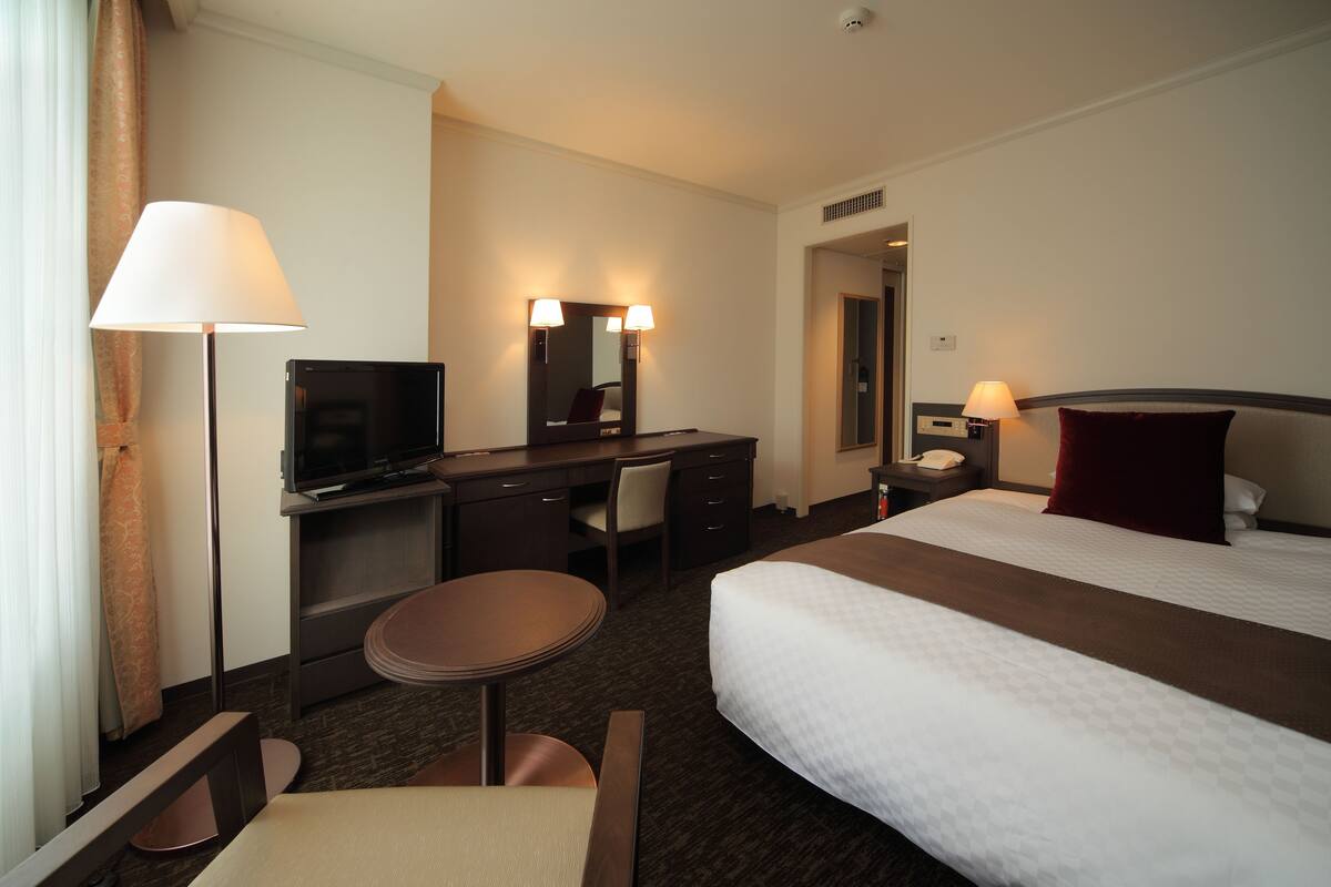 A hotel room with a bed, desk, chair, and a television.