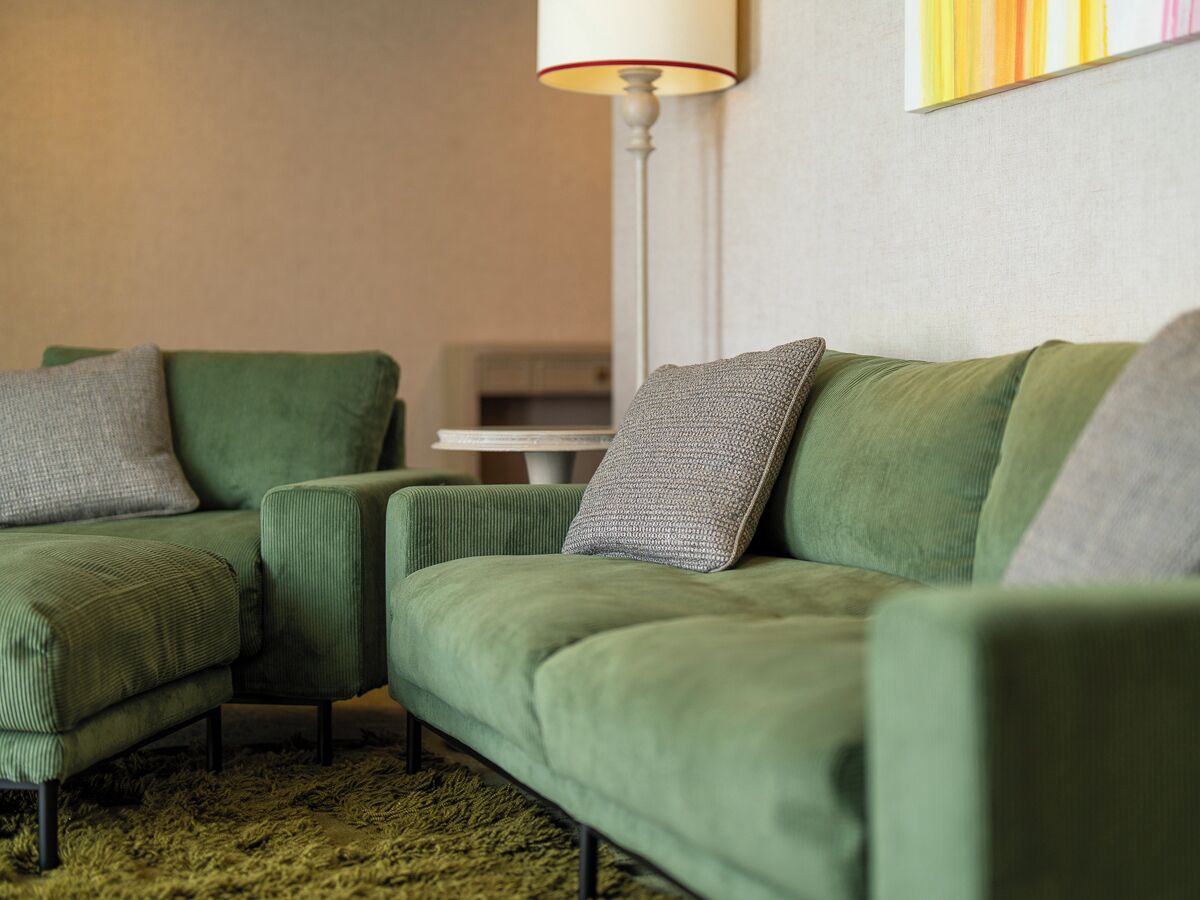 Ein grünes Sofa mit einem gemusterten Kissen, einer Stehlampe und einem Bild an der Wand.