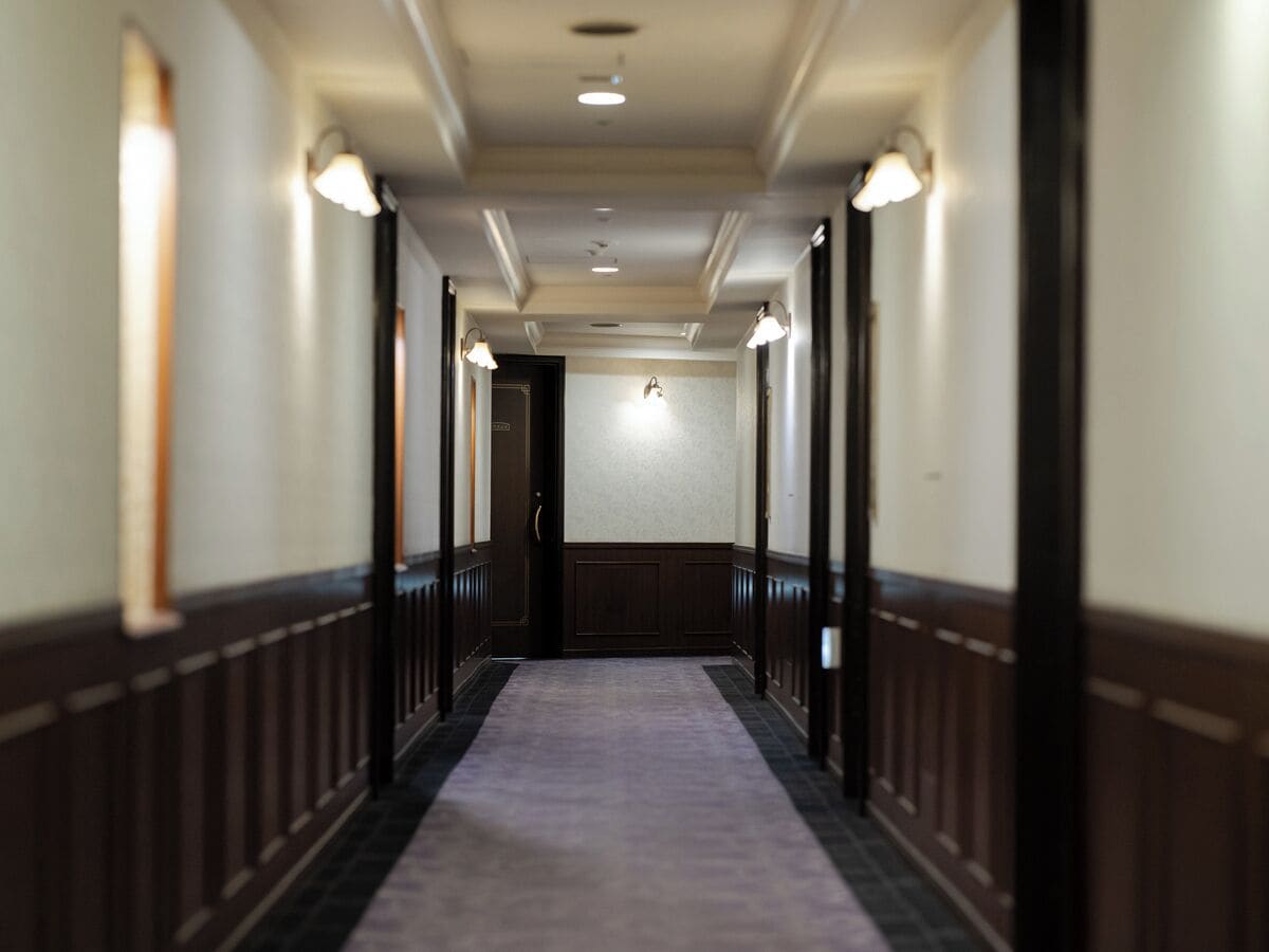 A hotel hallway with a carpeted floor, wooden paneling, and wall-mounted lights.